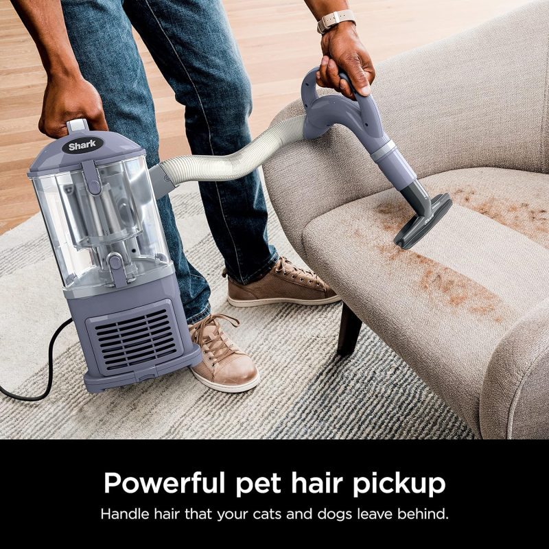 Person using a Shark vacuum cleaner with handheld attachment to clean pet hair from a couch