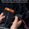Person using a portable jump starter on a dead car battery; device features black and orange design with USB outputs