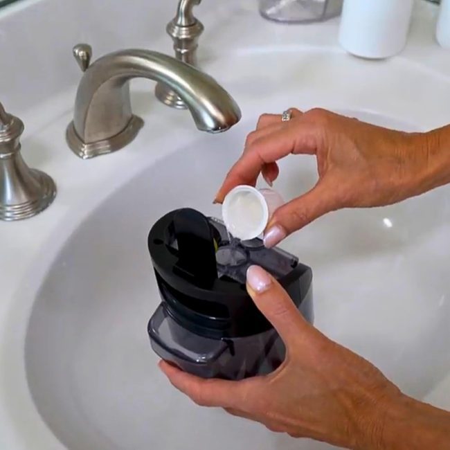 Person pouring liquid from a small cup into a black device over a sink