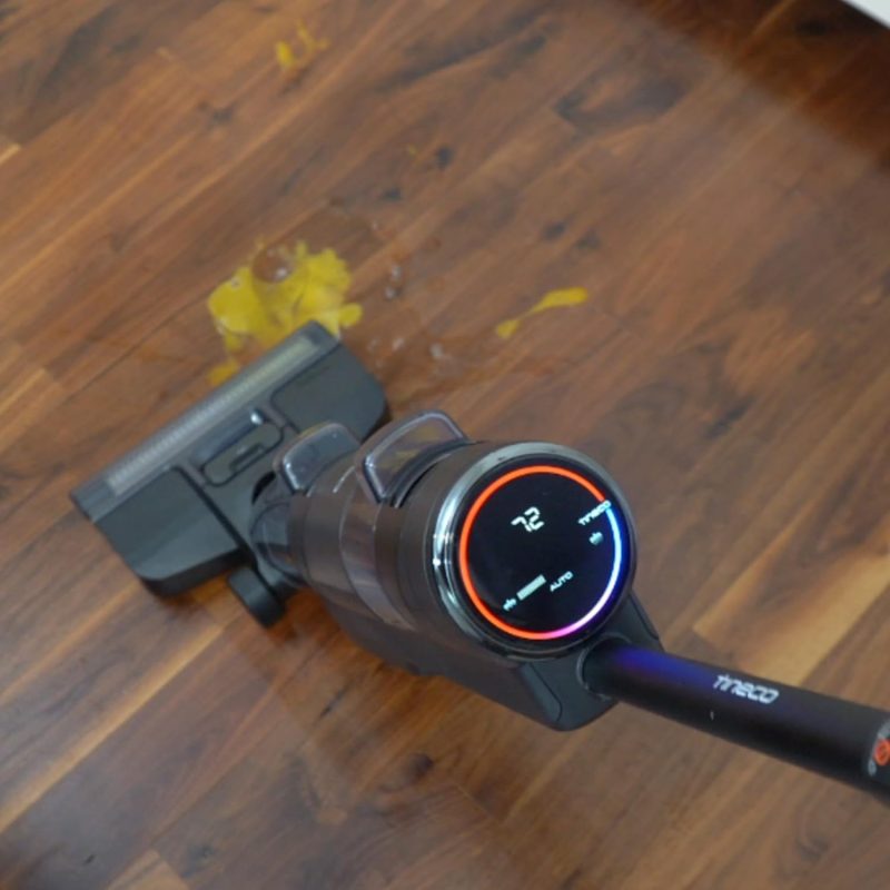 Vacuum cleaner on wooden floor with liquid spill and digital display showing 72