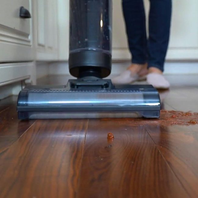 Vacuum cleaner removing debris from wooden floor with person in slippers operating it