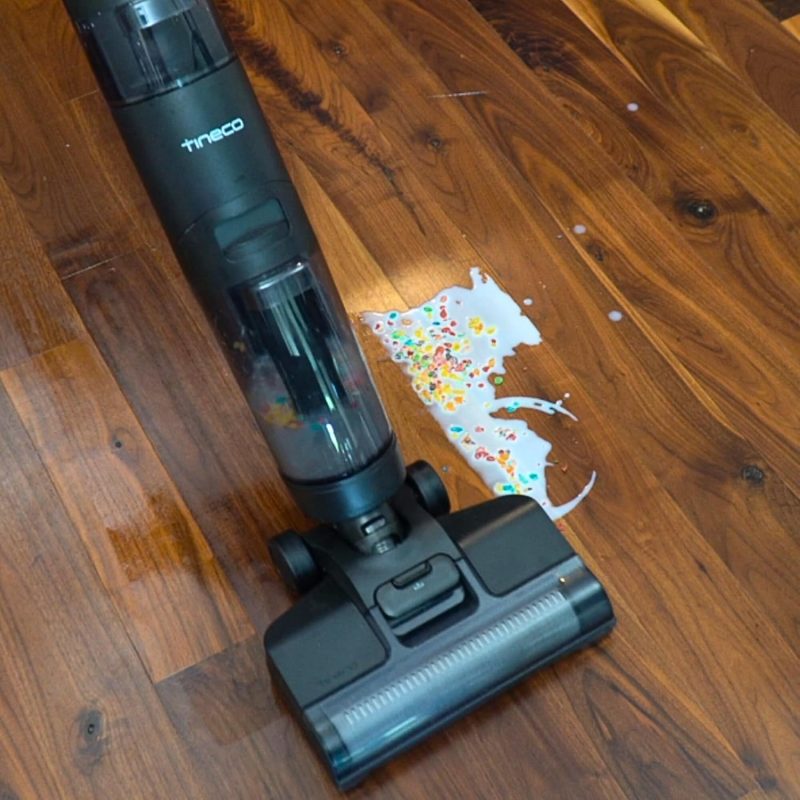 Vacuum cleaner efficiently cleaning colorful cereal and milk spill on wooden floor