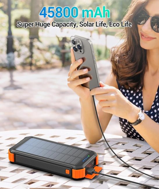 Woman using smartphone with portable solar power bank of 45800 mAh capacity outdoors