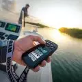 Hand holding a Minn Kota Terrova iPilot Link remote with boat helmsman in the background at sunset