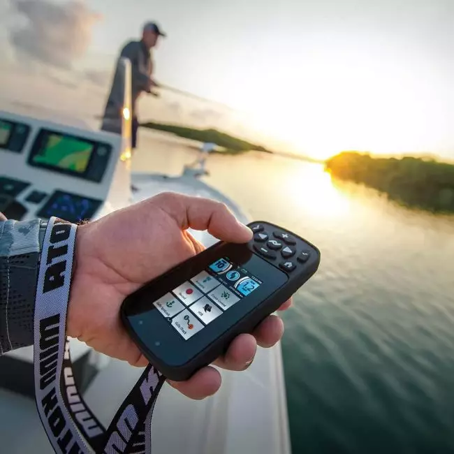 Hand holding a Minn Kota Terrova iPilot Link remote with boat helmsman in the background at sunset