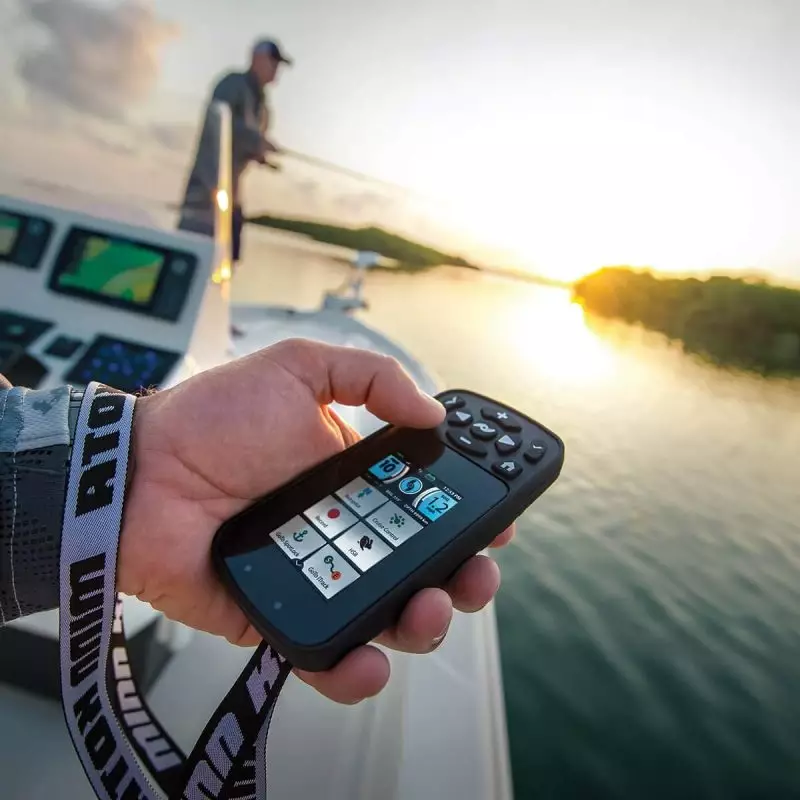 Minn Kota Terrova iPilot Link Remote Control in Use During Sunset Sailing Hand holding a Minn Kota Terrova iPilot Link remote with boat helmsman in the background at sunset