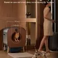 Automated cat litter box with a cat inside and dimensions displayed,   next to a woman with a suitcase