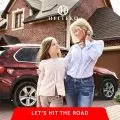 Mother and child smiling in front of their red SUV and brick house,   ready for a road trip,   with HELTEKO logo visible