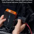 Person using a portable jump starter on a dead car battery; device features black and orange design with USB outputs
