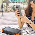 Woman using smartphone with portable solar power bank of 45800 mAh capacity outdoors